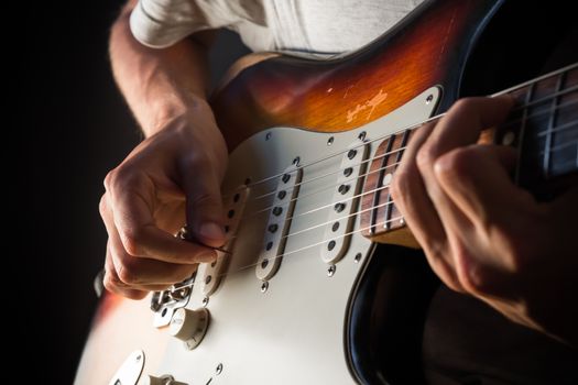 Closeup photo of male hands playing vintage electric sunburst guitar with mint pickguard with pick in front of dark background