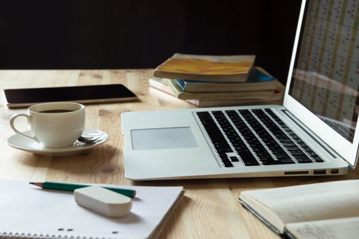 Home office working place with laptop, cup of coffee, notebook, textbooks,books, tablet on wooden table with dark background