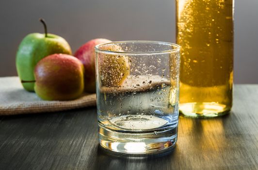An empty glass prepared to be poured with cold apple wine, apples in the background