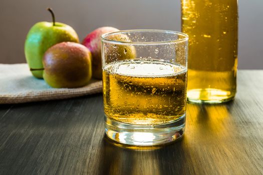 Aparkling apple wine in a glass in front of fresh apples and a bottle of apple cider on wooden rustic table