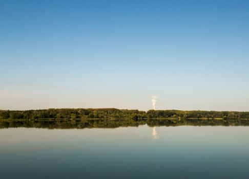 Lanscape image of a lake on a bright cloudless day with forest and a factory on lake's far end