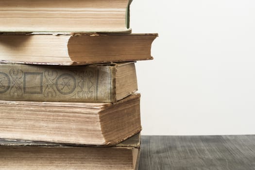 Stack of old books on dark wood table, in front of white background