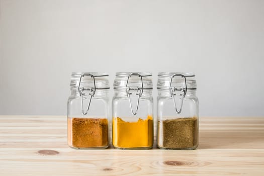 Three jars with eastern spices standing in row on light wood table