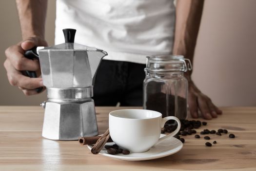 Male hands holding coffee pot ready to pour espresso in the white cup