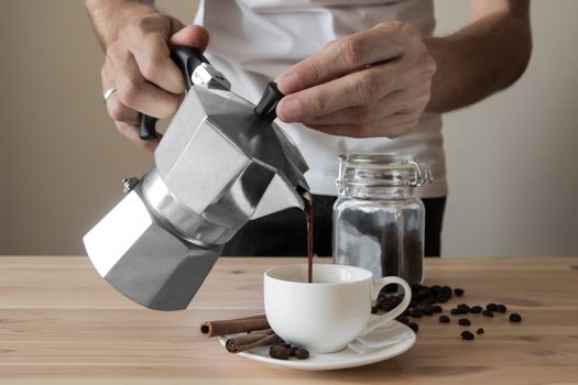 Male hands pouring coffee out of italian coffee pot in front of minimalistic background with coffee beans and cinnamon