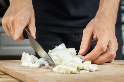 Onion and garlic cut with chef knife in kitchen by male hands