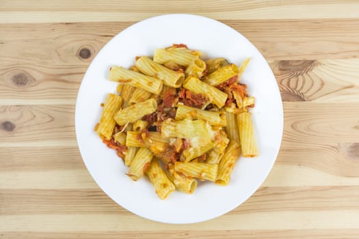 Top view of baked tortiglioni pasta with tomato sauce, mozzarella and parmesan cheese in the plate on the wood table