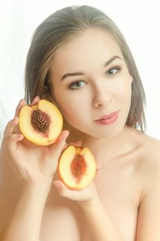 Beautiful girl with two peach halves in her hands on white background. Horizontal photo. Front view