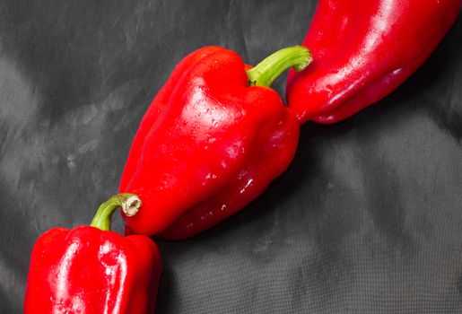 Three red peppers with green tail on a black background. Lie one by one