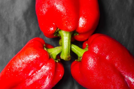 Three red peppers with green tail on a black background. Lie in front of each other