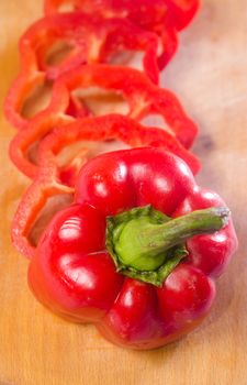 Red pepper cut by slice on a wooden background. Vertical photo
