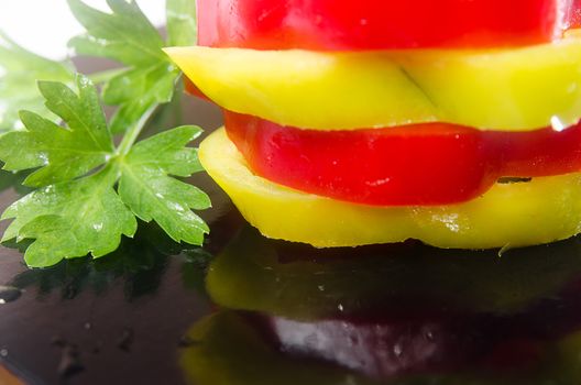 Sliced red and green peppers on a black background with parsley