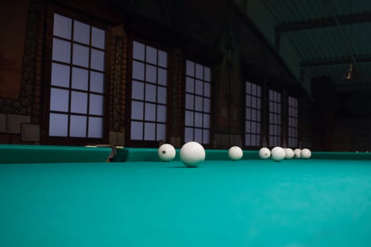 Russian billiards balls on green game table cloth in the middle of game with windows on background