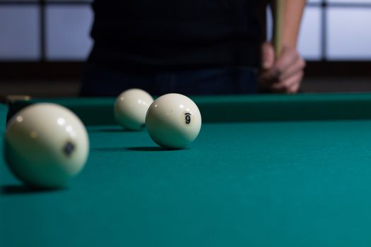 Close-up of Russian billiards game in process: three white balls on green game table cloth and player with cue on background