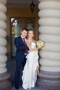 Stylish newlyweds embracing standing near the wall