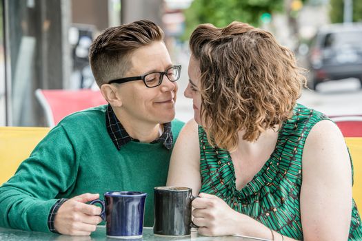 Romantic lesbian couple at bistro outdoors with coffee mugs in hand