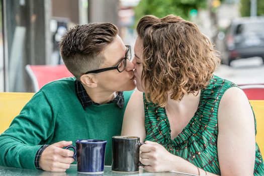 Cute young adult female couple kissing each other outdoors at bistro