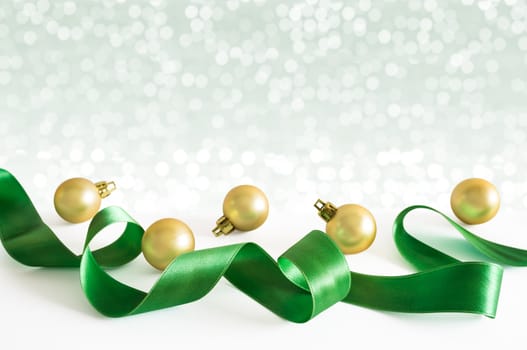 Golden christmas balls with green ribbon with lights snow winter background. Space for copy.