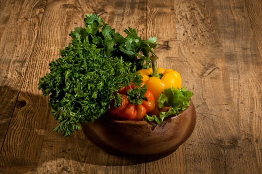 Red and yellow peppers and greenery in a wooden plate