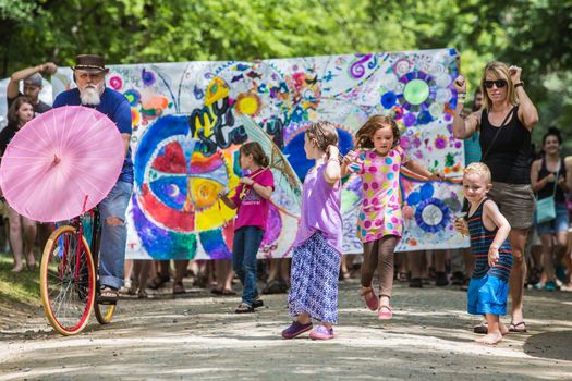 HOT SPRINGS, NC - JULY 10: Excited children adults walking down road with colorful banner and umbrella at the Wild Goose Festival on July 10, 2016 in Hot Springs, NC, USA.