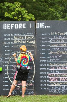 HOT SPRINGS, NC - JULY 7: Single woman in tie dye shirt writing on before I die list blackboard at the Wild Goose Festival on July 7, 2016 in Hot Springs, NC, USA.