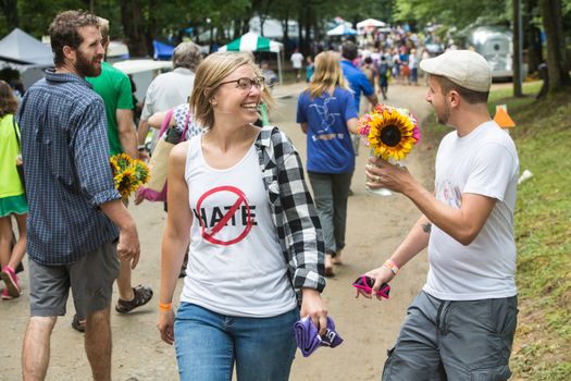 HOT SPRINGS, NC - JULY 8: Man in hat flirting with woman as he offers her a flower in the spirit of peace and tolerance at the Wild Goose Festival on July 8, 2016 in Hot Springs, NC, USA.