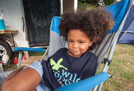 HOT SPRINGS, NC - JULY 10: Cute grinning little girl sitting in folding chair at the Wild Goose Festival on July 10, 2016 in Hot Springs, NC, USA.