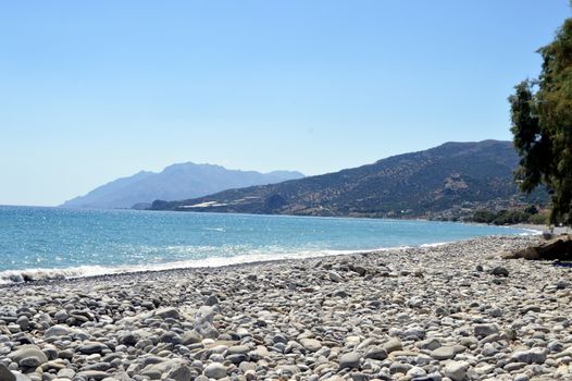 A fine sand beach with a hill, a blue sky and waves.