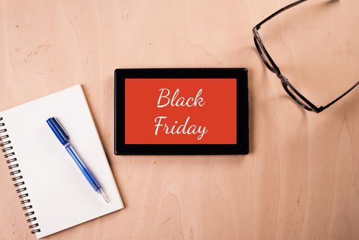 Digital tablet with the inscription: "Black Friday", the subject lay on a wooden table: glasses, Notepad, pen, conceptual illustration for shop advertising