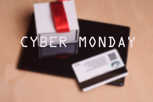 Background image, defocus, Credit card and electronic tablet on wooden table, gift with red ribbon, shopping online, inscription - Cyber Monday