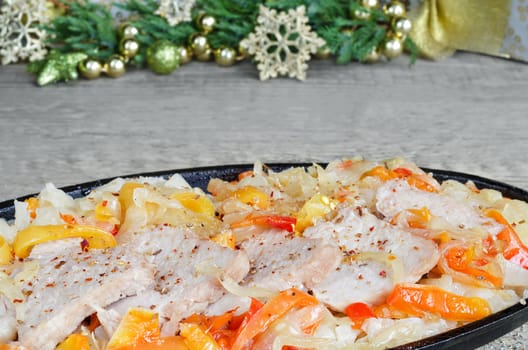 Sliced pork with vegetables in a frying pan. On wooden surfaces, and the backdrop of Christmas