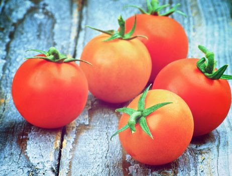 Arrangement of Five Fresh Ripe Red Cherry Tomatoes with Twigs on Rustic Wooden background. Focus on Foreground