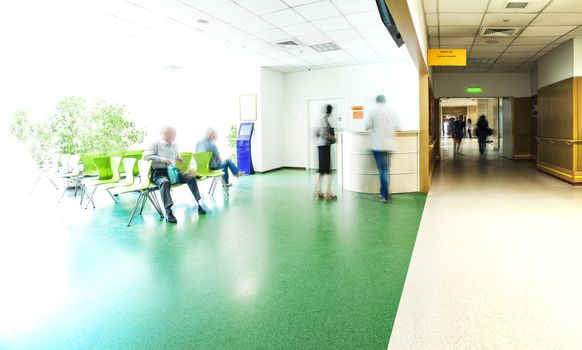 View of the registration desk, waiting area and a corridor in modern hospital with blurred figures of patients with a copy space.