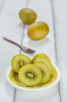 golden kiwi fruit and sliced on dish over white wooden background