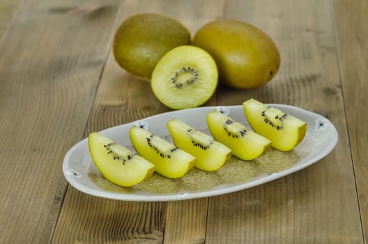 golden kiwi fruit and sliced on dish over wooden background