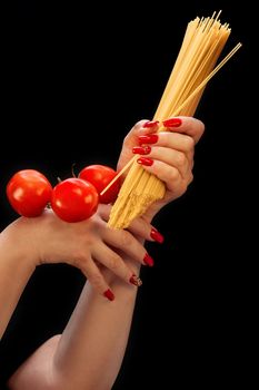 Female hands with beautiful manicure hold spaghetti and tomatoes on a black background