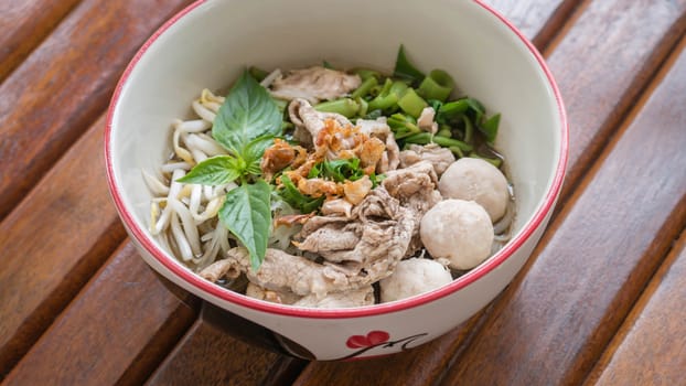 Asian white noodles with pork and vegetables in bowl over wooden background