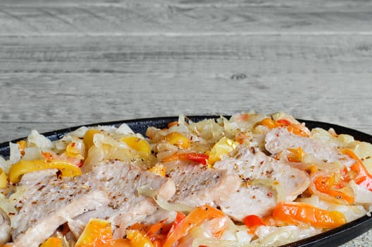 Sliced pork with steamed vegetables on the pan,on the gray wooden surface. Plenty of space for inscriptions.