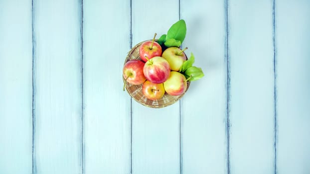 Top view red and yellow apple with leaves and  bamboo basket on  white wooden background with free space for text