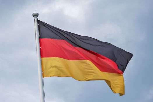 The flag of Germany flutters on wind against the background of gray clouds.