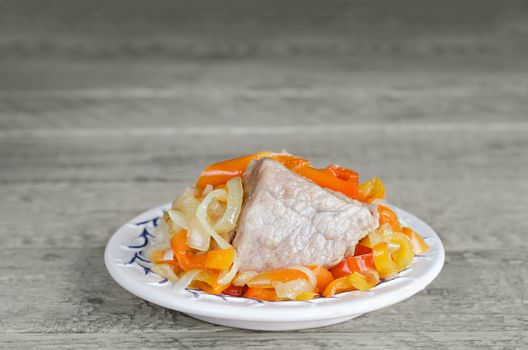 Piece of pork with steamed vegetables on the plate, on the grey wooden surface. Plenty of space for inscriptions.