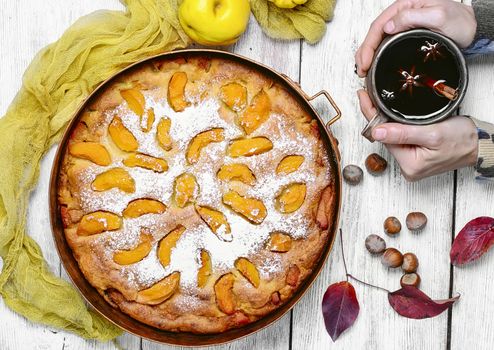 Warm aromatic tea in hand and pie with autumn quince