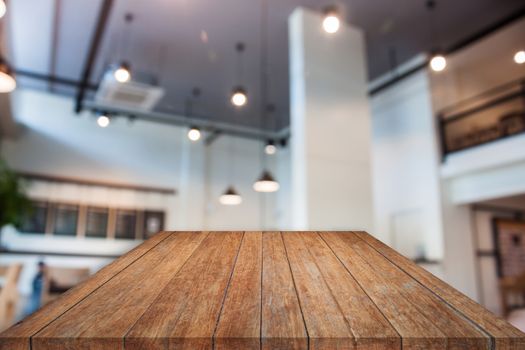 Perspective brown wooden table top with abstract blur coffee shop interior for background