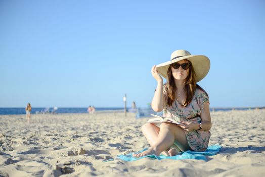 Portrait of a young brunette relaxing on the beach, reading a book. Summer time