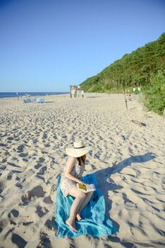 Portrait of a young brunette relaxing on the beach, reading a book. Summer time