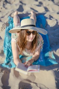 Portrait of a young brunette relaxing on the beach, reading a book. Summer time