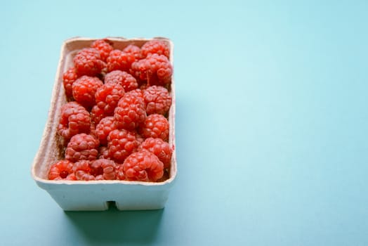 box of fresh raspberries on a blue background