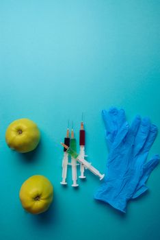 Chemical additives in food or genetically modified fruit concept. Green apple with syringes of chemicals. Isolated on blue background.