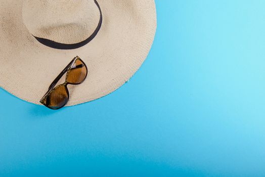 Straw hat and sunglasses on blue background. beach equipment.