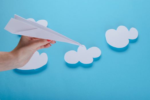 Paper plane in female hand on a blue background with clouds